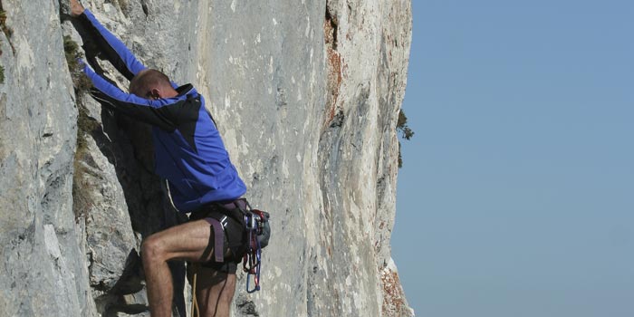 Guy climbs up a vertical rock face